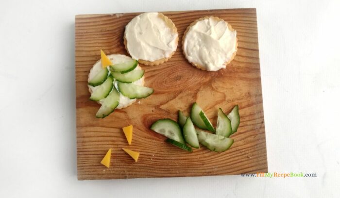 cucumber and cheese decoration, for Simple Christmas Cracker Appetizers recipe ideas for snacks and treats. Crackers garnished with cream cheese, salami, cucumber, cherry tomato.