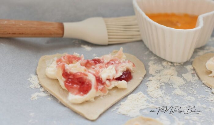 adding the cream cheese and jam on top of the heart shaped puff pastry cut outs, leaving a small edge to paste some egg wash before adding to the baking tray, and baking. snacks that are so simple and easy.