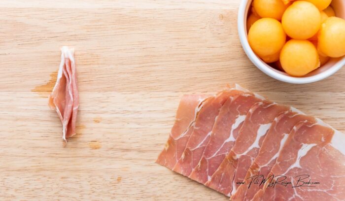 Cut the prosciutto slices in half. Then take a strip of prosciutto and fold it accordion-style, creating a bow-like pattern. This folding technique adds texture and visual appeal to the appetizer.