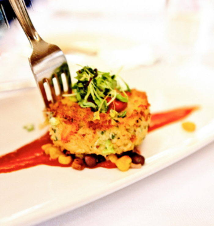 Crab Cake with Tomato Butter Sauce recipe plated for a gourmet fine dining dinner. Easy dish to serve for a meal set on corn salad.