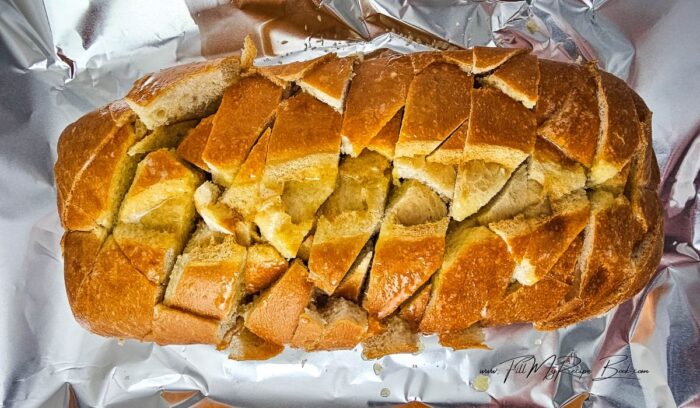 Place the bread on a large sheet of foil on a baking sheet. Cut diagonal slices into the bread, stopping before you cut completely through